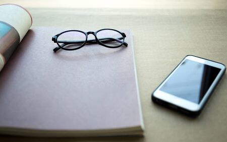 Focus on glasses with cell phone and book on brown paper backgroundの写真素材