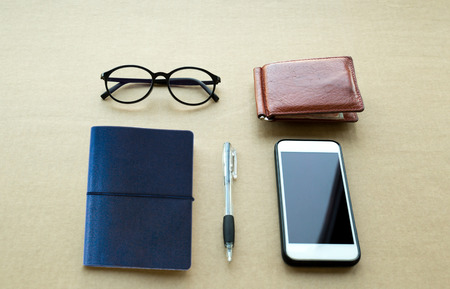 Concept Everyday life object needs object notebook and pen ,cell phone and glasses on brown paper backgroundの写真素材