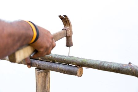 Man hands nails with hammer on wooden outdoors making a fence in white background
