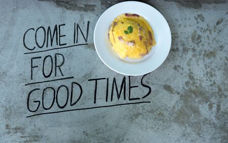 Omelette on rice with ham and bacon with word on concrete floor