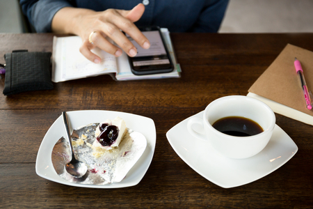 Selected focus woman using cell phone and having blueberry cake with coffee on wooden tableの写真素材