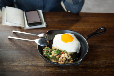 Woman with cell phone having stir fried chicken chilli and thai basil with fried egg on top in restaurantの写真素材