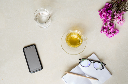 Top view cup of tea with flower , cell phone, glass of water and glasses with pencil on tiled floor backgroundの写真素材