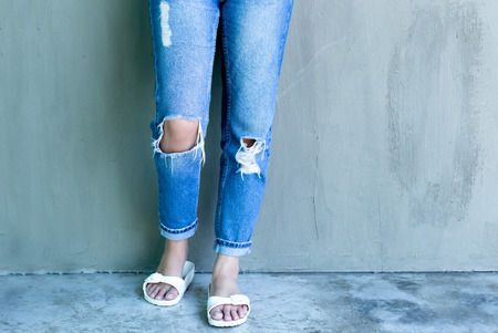 Young woman fashion with ripped jeans and flip flop with concrete wall in backgroundの写真素材