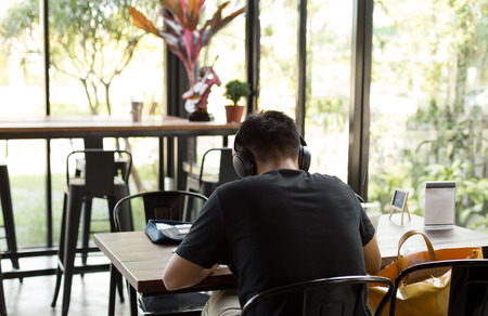 Asian student studying in  the cafe with headphones listening to music