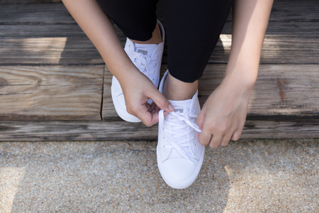Young woman tie shoelaces on white sneakers on wooden deckの写真素材