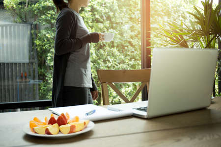 Businesswoman holding coffee with fresh fruit and laptop on tableの写真素材