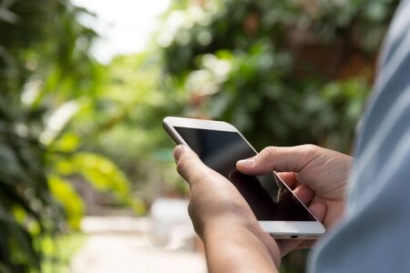 Woman hand using cell phone with blur garden in backgroundの写真素材