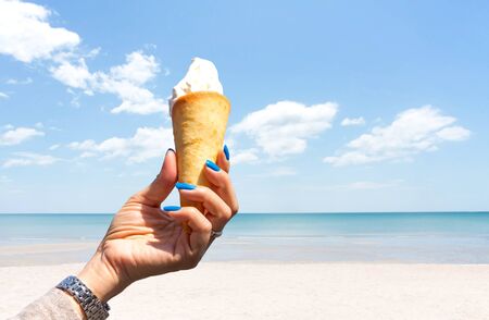 Hand holding ice cream cone on the beach with blue sky and cloudの写真素材