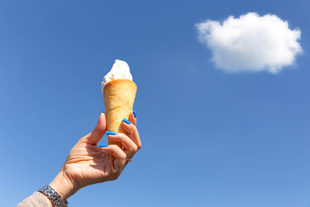woman hand holding ice cream cone with blue sky and cloud in backgroundの写真素材