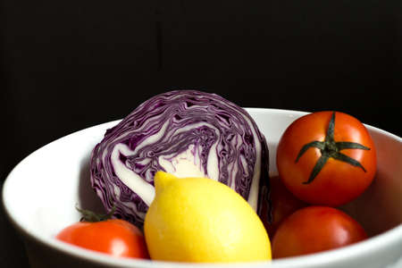 Red cabbage cut in half in white bowl with lemon and tomato isolated in black backgroundの写真素材