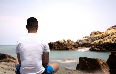 Man sitting on the rock doing meditation by the sea in day timeの写真素材