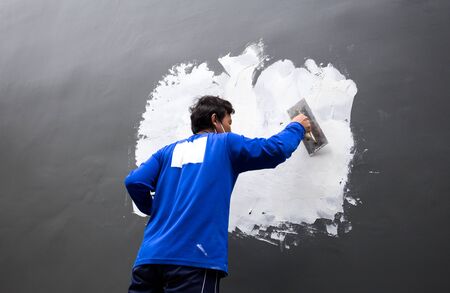 Builder plastering grey concrete at wall with white plaster on building siteの写真素材