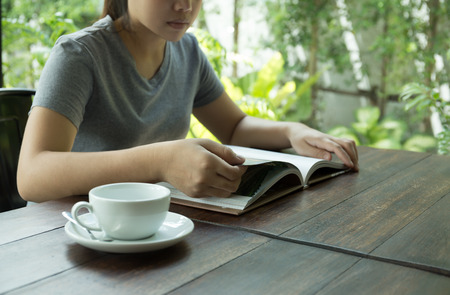 Young woman sitting on table reading a book with cup of coffee in cafe shopの写真素材