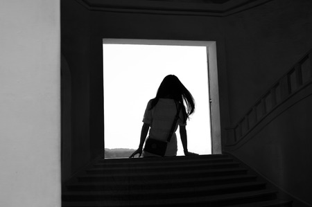 silhouette teen girl sitting on door step thinking in black and white backgroundの写真素材