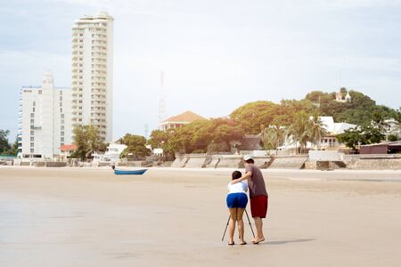 Couple taking picture using tripod on the beach on vacationの写真素材