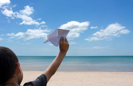 Little boy playing with a paper plane on the beach with blue skyの写真素材