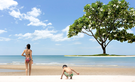 Mother and Sons playing on the beach white sand and beautiful frangipani tree and calm ocean in blue skyの写真素材