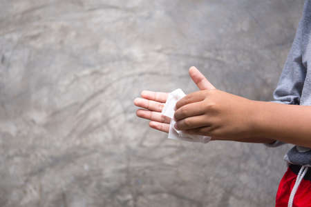 Young boy cleaning his hands with wet wipe before having food in gray backgroundの写真素材