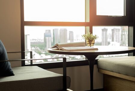 Wooden table with an opened book and plant on window with sunlight and city viewの写真素材