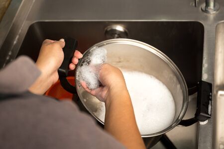 Woman hand washing stainless steel pot with dish washing soap in kitchen sinkの写真素材