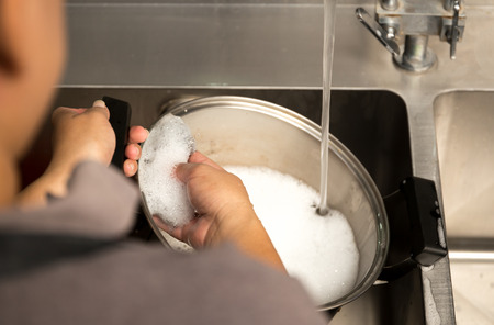 Woman hand washing stainless steel pot with dish washing soap in kitchen sinkの写真素材