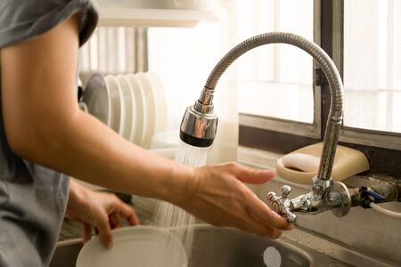 Woman's trun on tap water doing washing dishes in kitchen sink at homeの写真素材