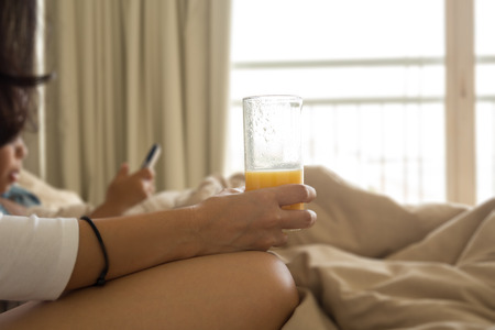 Mother holding glass of orange with son playing cell phone on bed in the morningの写真素材