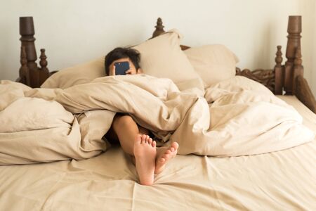 Little boy lying on a bed bare foot playing cell phone relaxingの写真素材