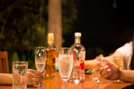 Group of friends enjoying drinking a glass of champagne and whiskey at party at nightの写真素材