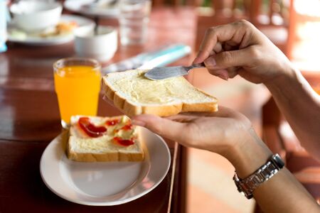 Breakfast with woman hand spreads butter on slice of bread and orange juice on the tableの写真素材