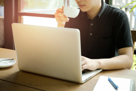 Selective focus on coffee cup man working on laptop and holding cup of coffee in cafeの写真素材