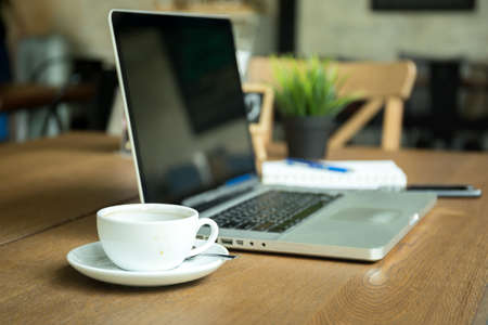 Selected focus cup of coffee with notebook and cell phone cup on wooden deskの写真素材