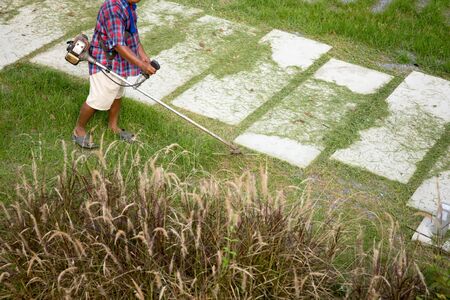 Senior worker mows grass in the yard with electric hand trimmer in the garden