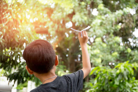 Little boy playing with a paper plane in the garden with sunlight