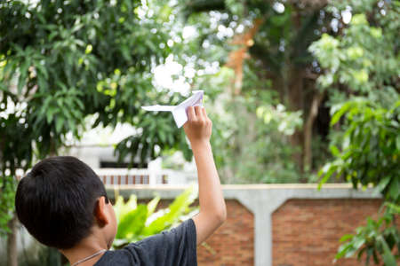 Little boy playing with a paper plane in the garden