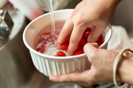 Hands washing fresh cherry tomatoes in running water in kitchen sinkの写真素材