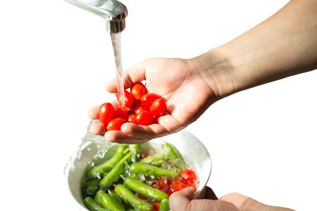 Hands washing fresh cherry tomatoes in running water isolated in white backgroundの写真素材