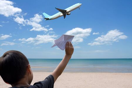 Little boy playing with a paper plane on the beach with plane in the airの写真素材
