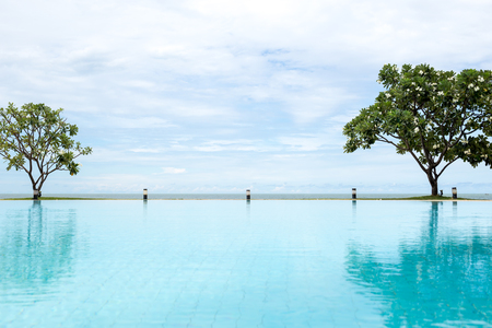 Swimming pool with  Plumeria tree and blue sky and ocean in tropical landscapeの写真素材