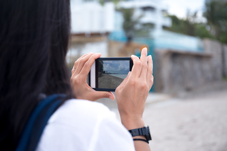 Woman traveler taking picture of the beach with cell phone on vacationの写真素材