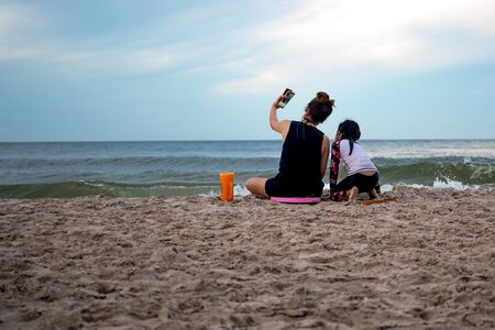 Mother and daughter enjoying vacation taking picture on cell phone by the beach in Thailandの写真素材