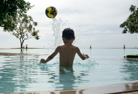 Little boy playing a ball in swimming pool in summerの写真素材