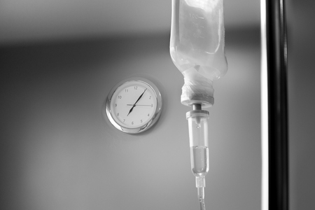 Saline solution drip for patient with wall clock in hospital in black and whiteの写真素材