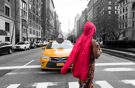 Woman tourist in red waterproof cloth crossing the road with yellow taxi at traffic light in New York Cityの写真素材