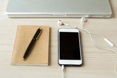Cell phone with headphone and notebook with  pen and laptop on wooden tableの写真素材