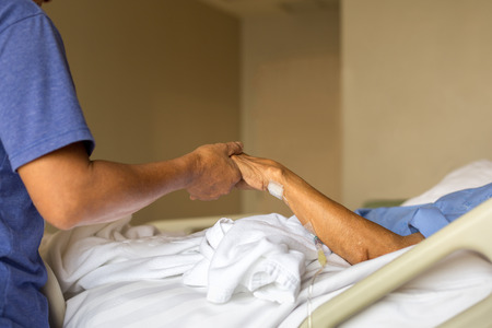 Son holding father is hand in bed in hospital health careの写真素材