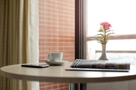 Conceptual cup of coffee with newspaper and cell phone on wooden table in morning lightの写真素材