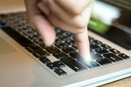 Conceptual people finger put the enter button on laptop keyboard with light flareの写真素材