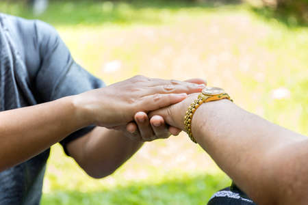 Elderly woman in wheelchair holding hands with caregiver in open airの写真素材